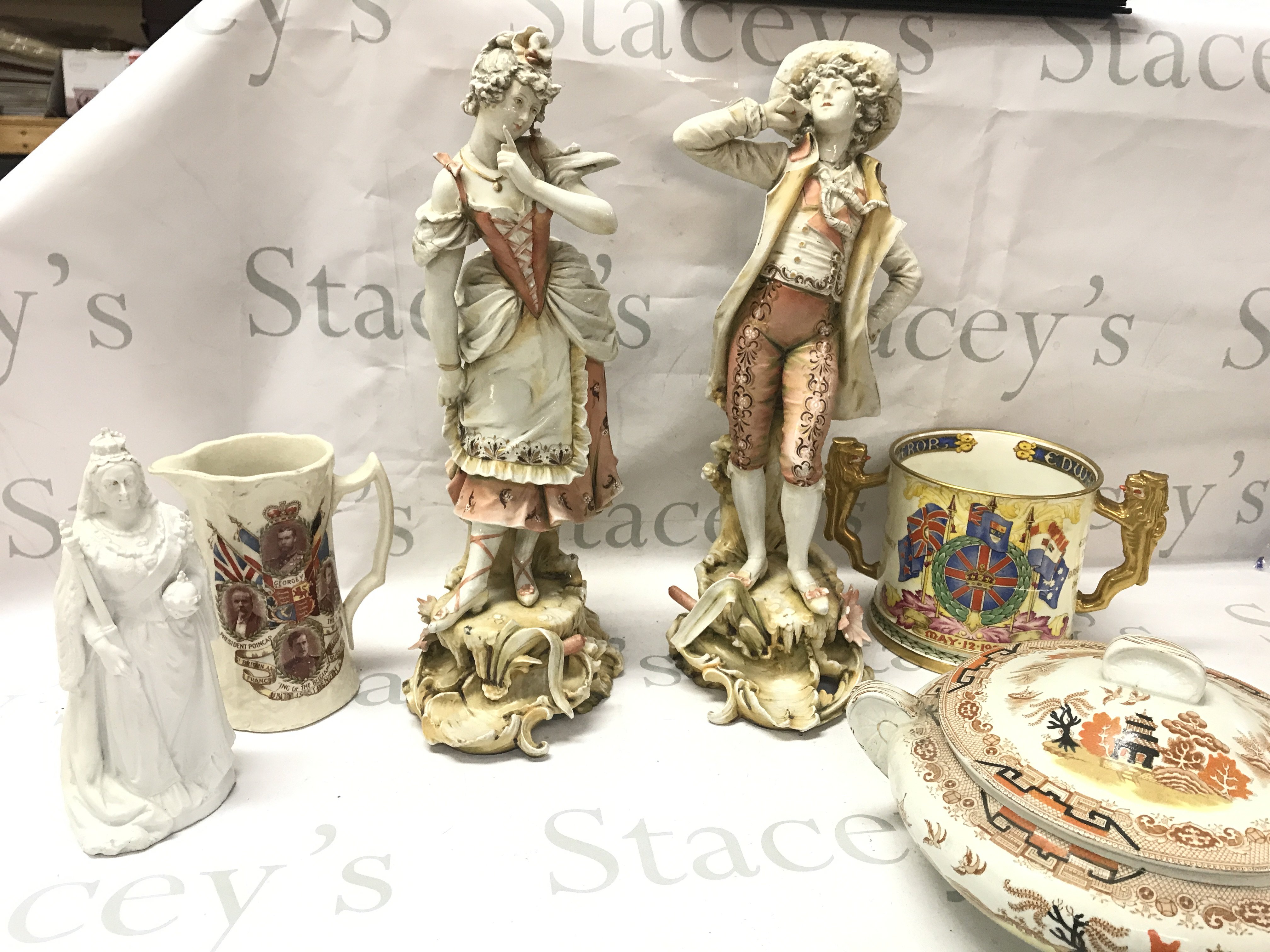 Two classical couple porcelain figures, Queen Victoria figure, Commemorative cups (twin handled by Paragon), Derwent Gibsons tureen . This lot cannot be posted
