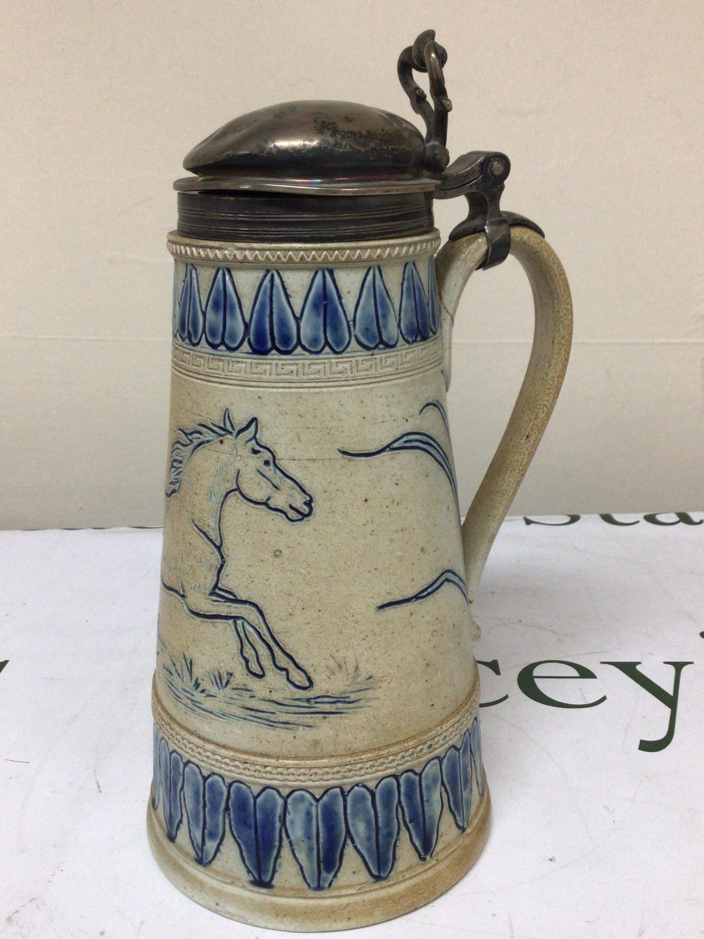 A Lambeth Doulton Victorian stoneware jug with a silver hinged top the sides with horses and a repeat pattern boarder. damage to the handle Hight 26cm marks to the base.