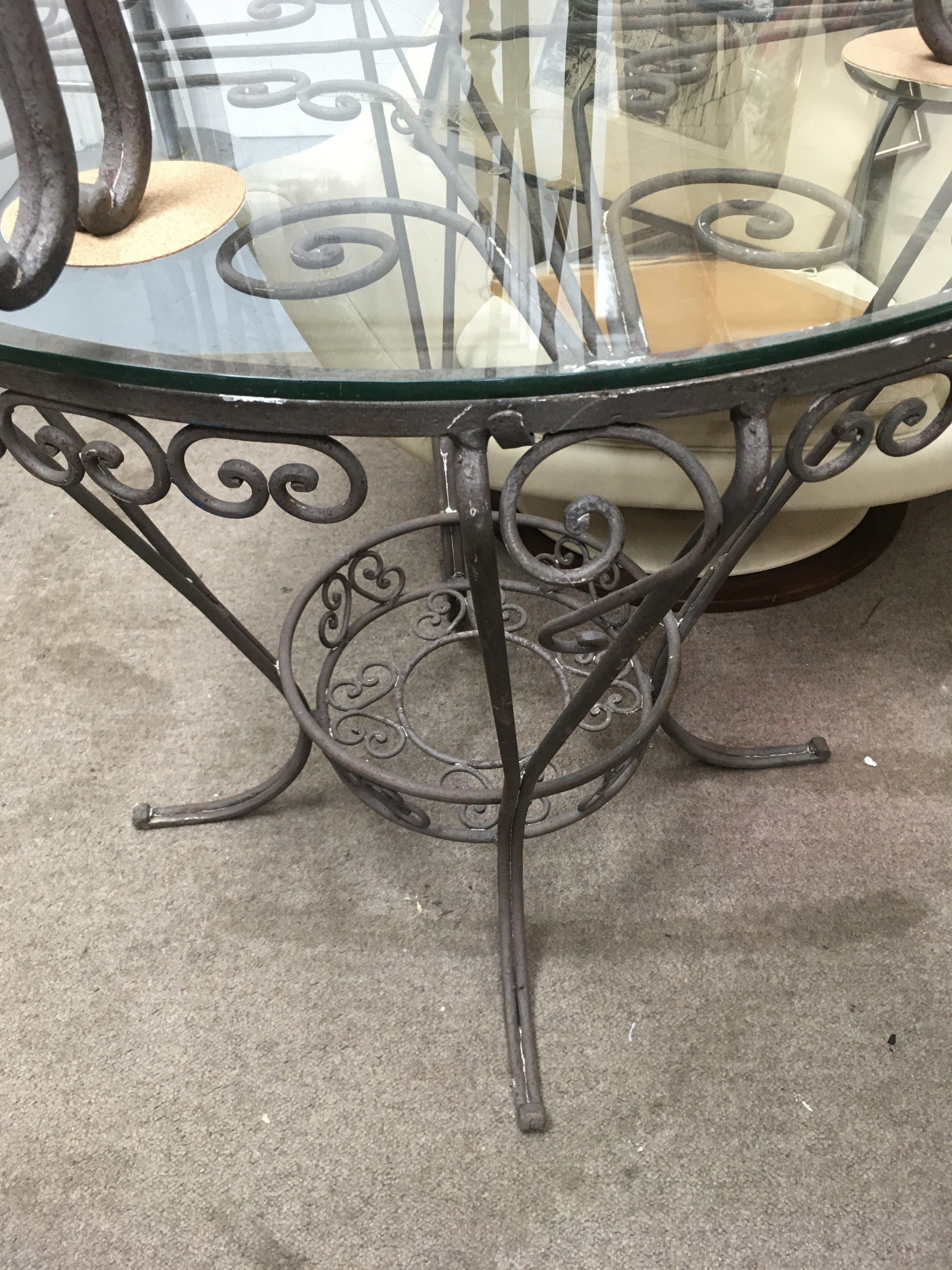 A circular metal garden table with glass top with four chairs