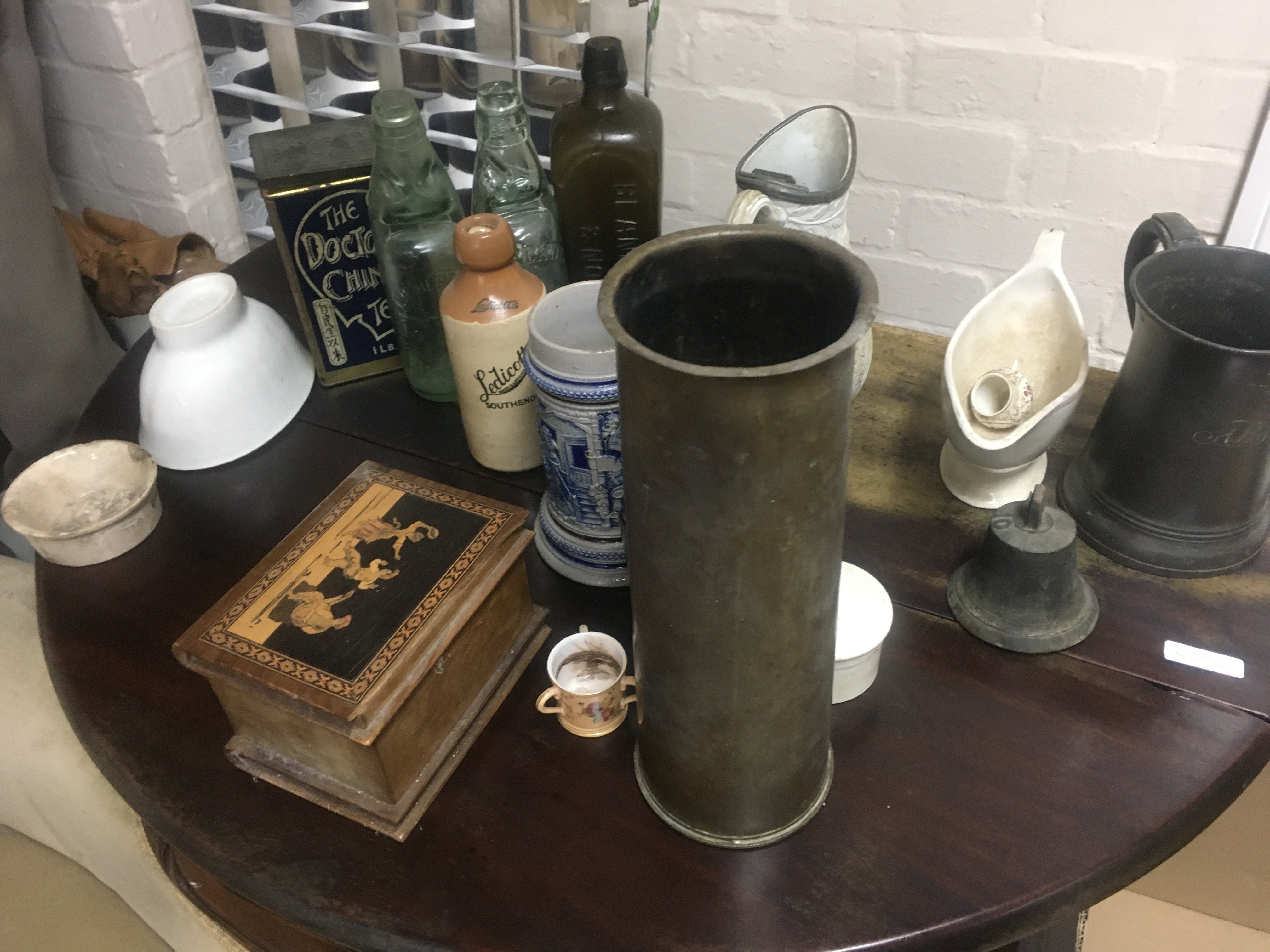 A box containing glass bottles advertising various ceramics and a pewter jug.
