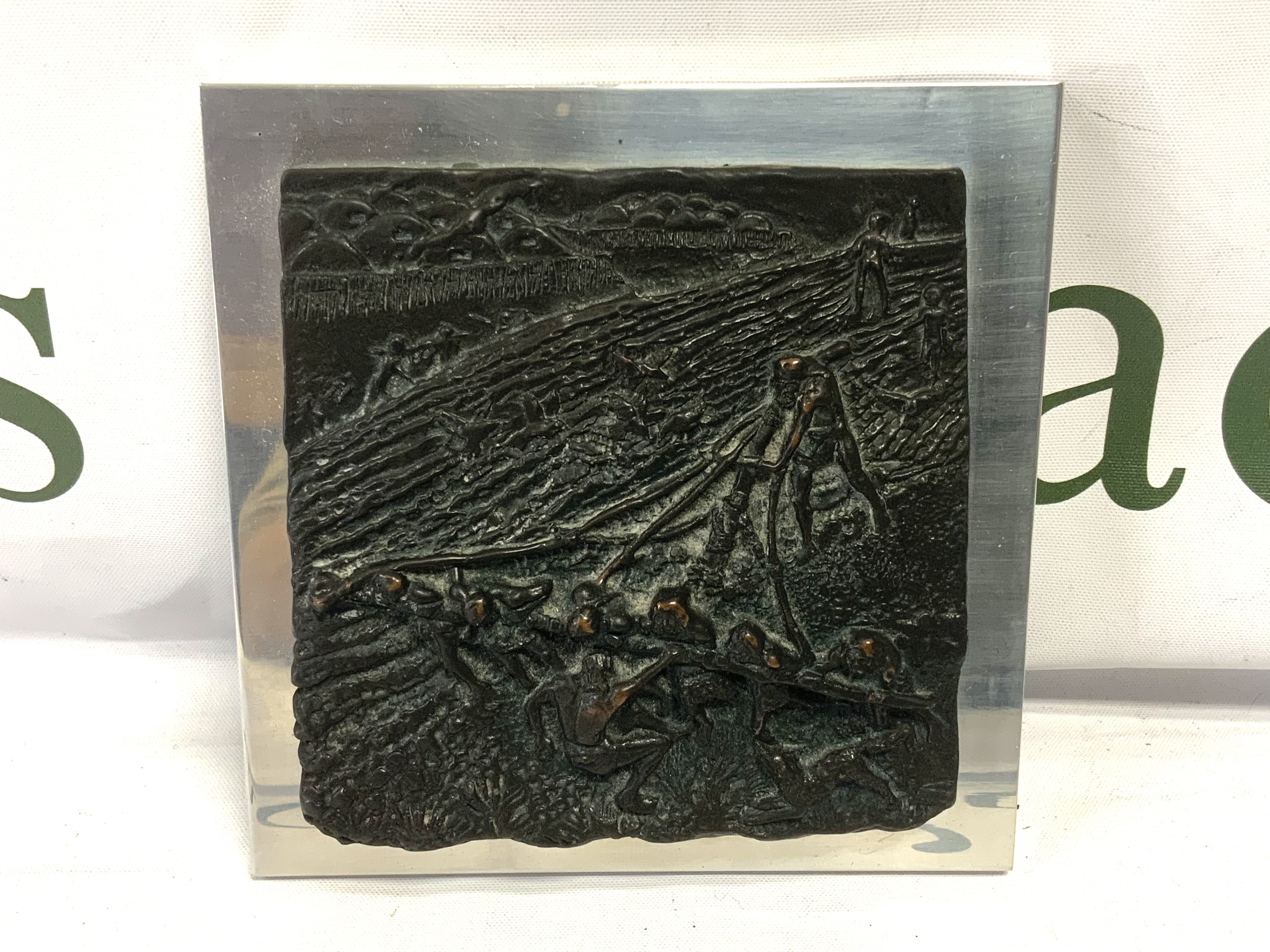 A small Bronze plaque depicting a farming scene, mounted 12.5cm x 12.5cm.