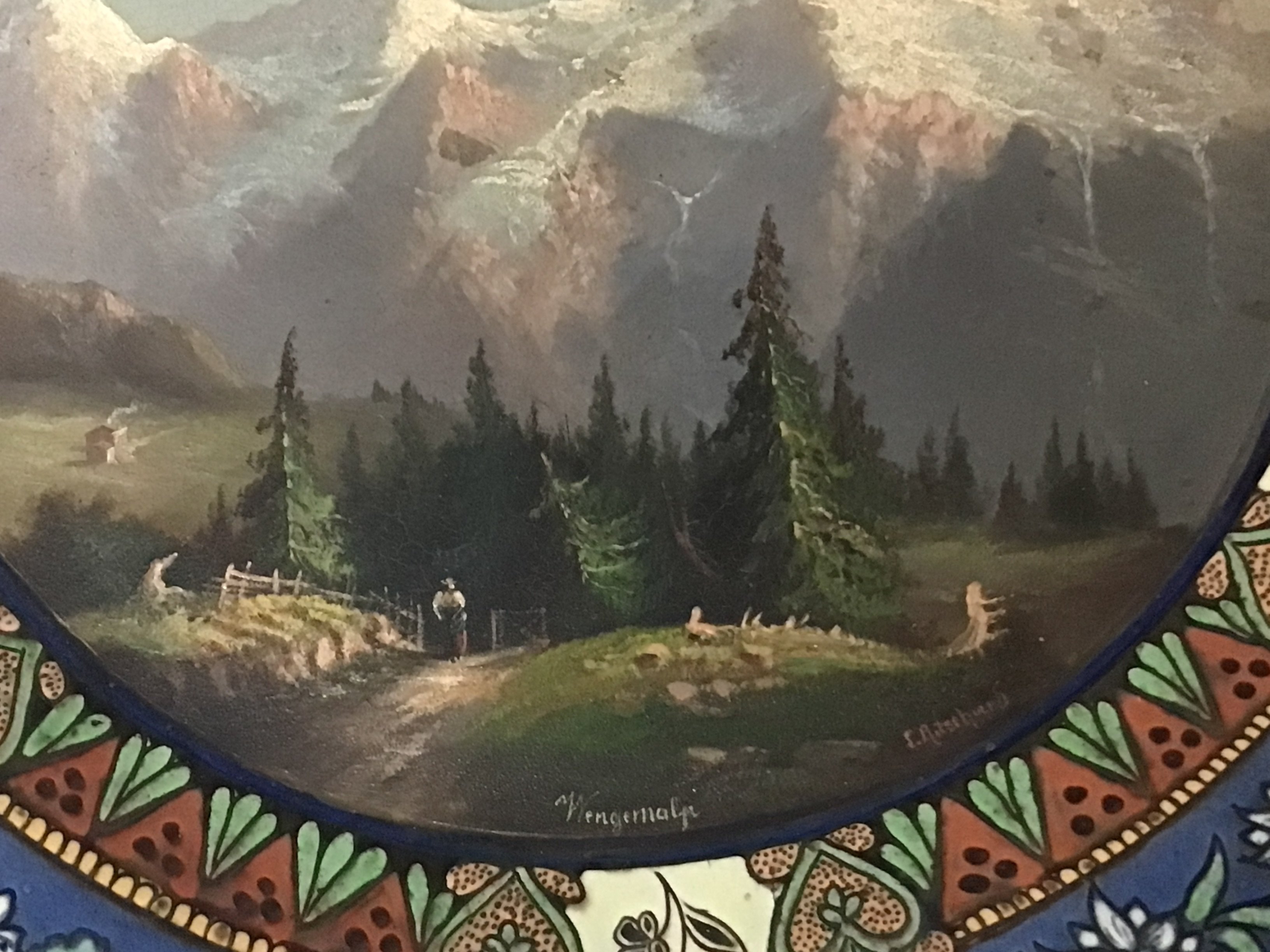 A quality ceramic Continental wall plaque hand painted with Tyrollean view with snow caped mountains and figures signed and with makers name to the reverse no obvious damage. 39cm wide.- NO RESERVE