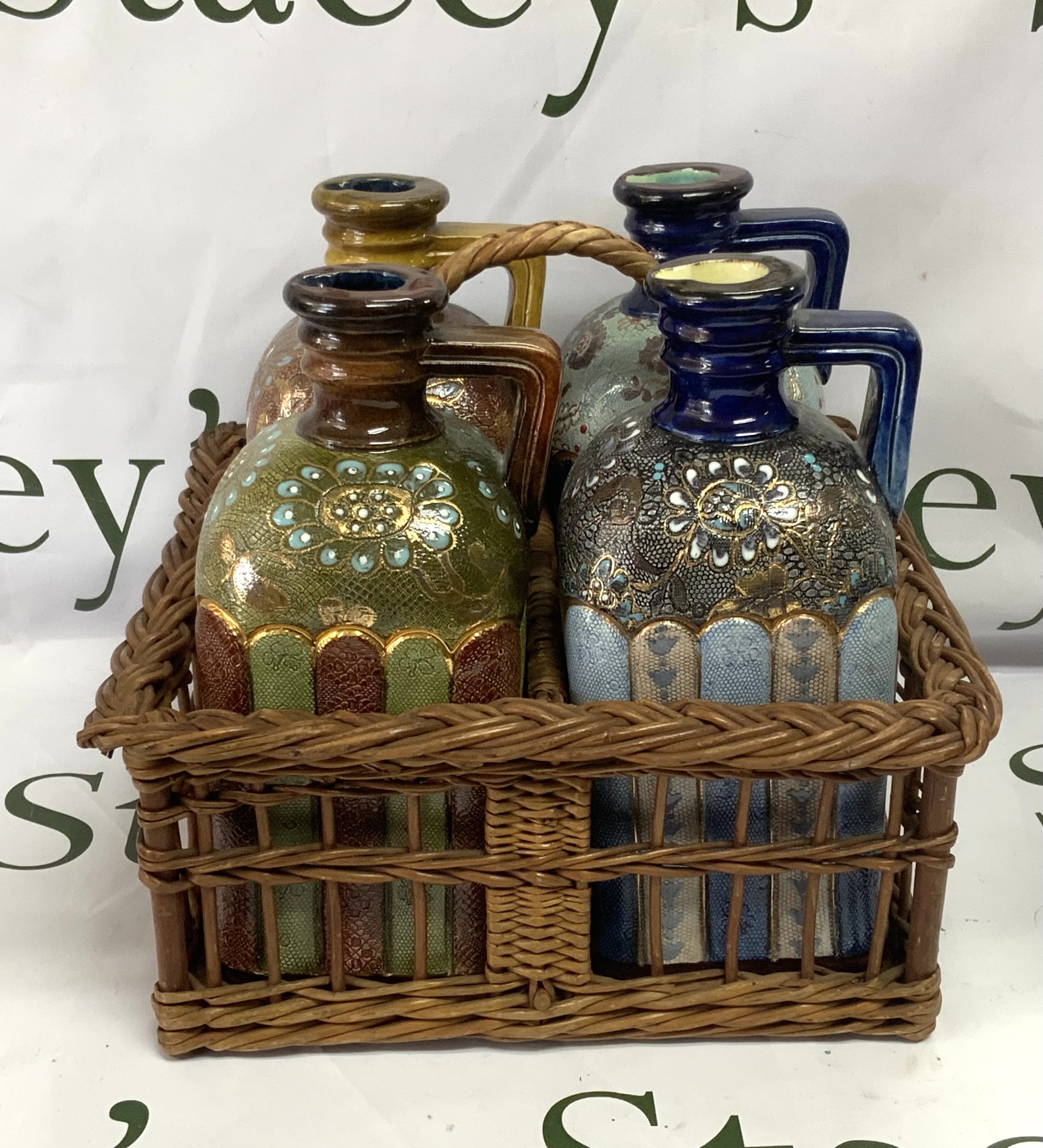 A set of 4 varied design Doulton Lambeth stoneware brandy flasks, circa 1880, square section shouldered form with angled strap handle, decorated with applied foliate bands, impressed marks, each 21cm high. Complete with wicker basket with handle. (No visable damage or restoration). Cat D, postage not avaliable for this lot.