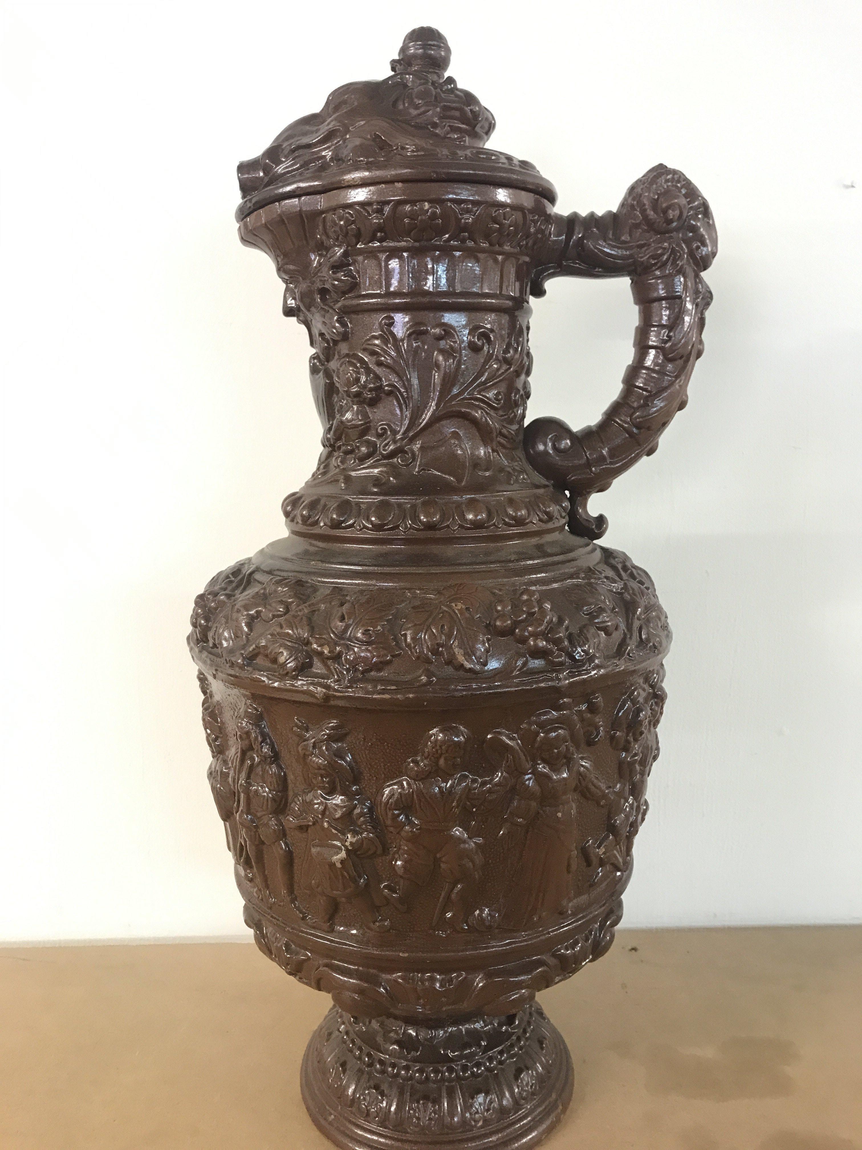 A German pottery ewer, Metilach style decorated with classical style figures and animals. 53cm tall approximately .This lot cannot be posted