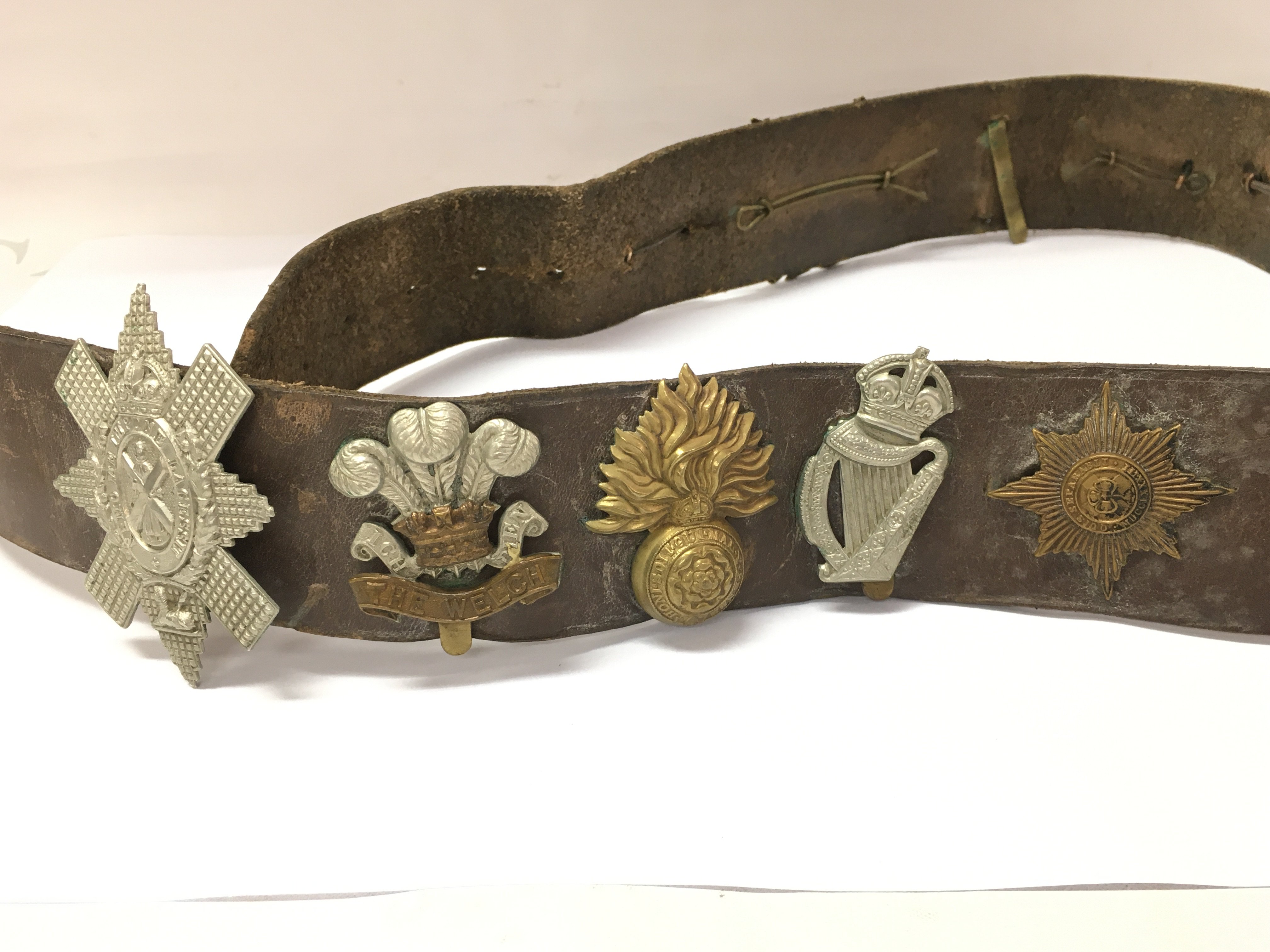 A collection of assorted cap badges fixed to a vintage belt. Postage B