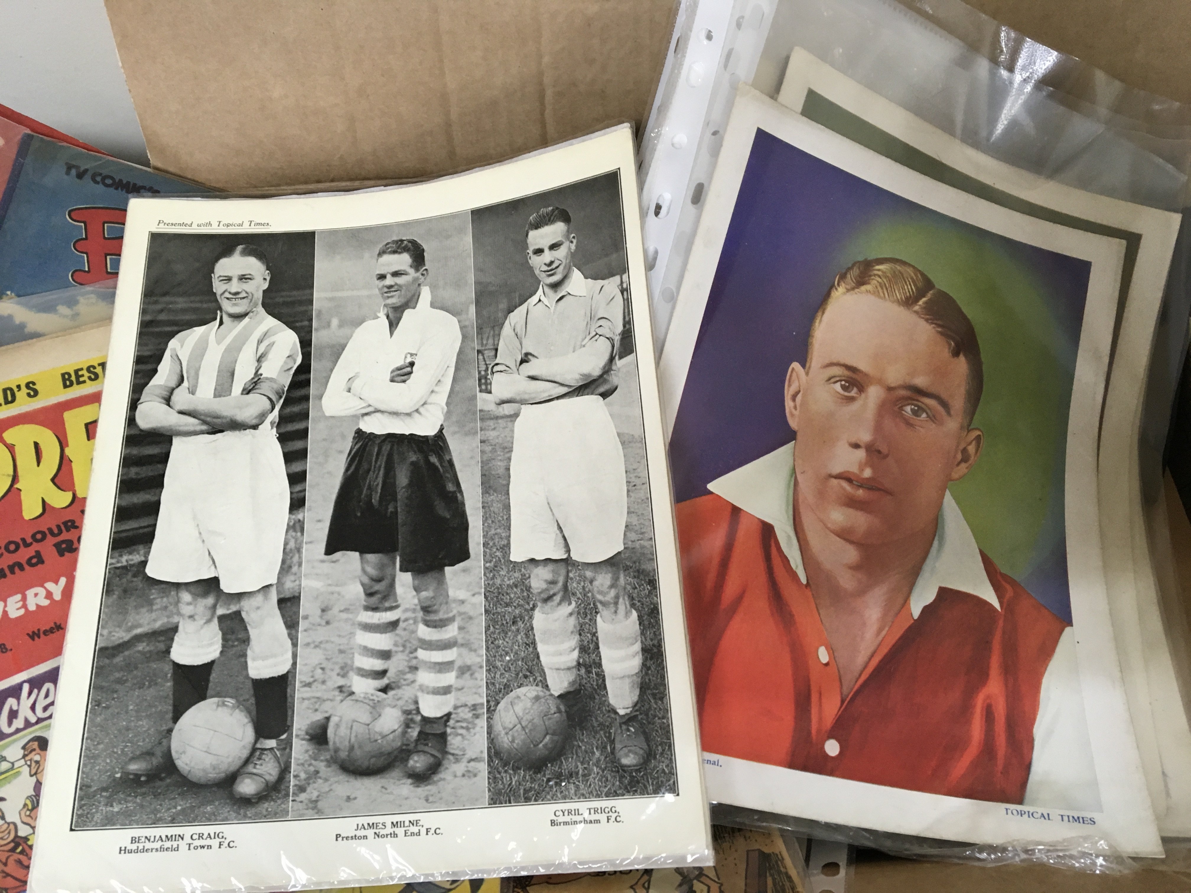 A box containing ephemera including some first issue comics TV Help issue one Vintage Topical Times football players Vintage Champion and lots of other ephemera.