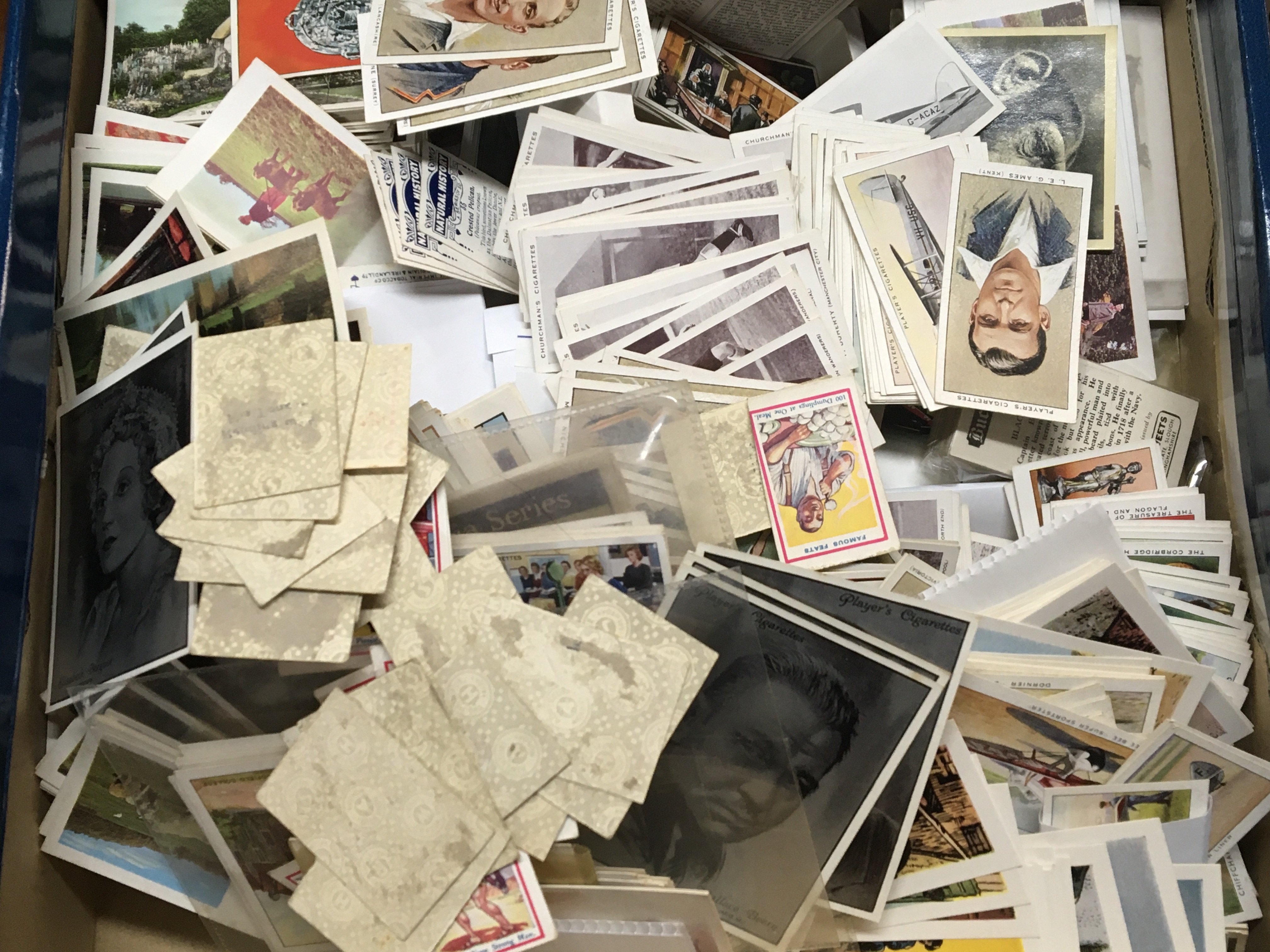 A box containing a collection of loose vintage cigarette cards and other cards.
