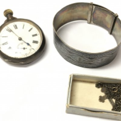 A silver cased pocket watch with a silver bangle and chain and cross pendant and a silver crest.