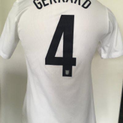 Steven Gerrard England Match Worn Football Shirt: White short sleeve shirt with number 4 Gerrard to rear. Front has number 4 and gold emblem below 3 Lions stating 150 years 1863 - 2013. Worn v Denmark in a friendly at Wembley on 5 3 2014. Photograph of Gerrard wearing the shirt which has matching stains.