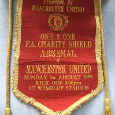 1999 Arsenal v Manchester United Charity Shield Exchange Pennant: Quality, embroidered 15 inch pennant given by Manchester United captain Denis Irwin to Arsenal captain Nigel Winterburn. Picture of the pennant in Winterburns hands with officials after the coin toss, signed by both players. Also a signed picture of Irwin with pennant in hand meeting dignitaries. Pennant reads Presented by Manchester United with club badge underneath. Below that it has match details embroidered in gold with red background. One off rare item. Manchester United had just completed the treble.