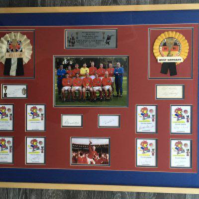 England 1966 World Cup Signed Display: Stunning large, quality display with an autograph of all the winning 11 plus Alf Ramsey. 8 autographs are on World Cup Willie signed cards with both Charltons, Moore and Ramsey on white cards. Original rosettes of England and Germany A team group photo and plaque. Expensively framed in red and blue which sets the white cards off nicely. Alan Ball beginning to fade. Measures 38 x 28 inches.