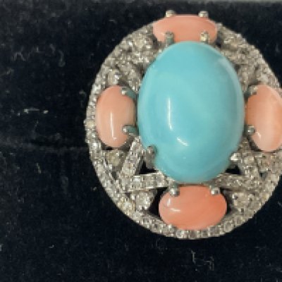 Large oval dress ring in white metal set with a central cabochon turquoise, 4 cabochon turquoise, 4 cabochon pink coral and mixed and rose cut diamonds, boxed. Turquoise 5.28ct. Coral 2.00ct. Diamonds 0.50ct. Ring size approx M. Postage catagory A.