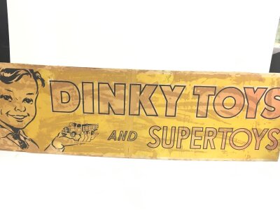 A Vintage Dinky Toys,Ply Wood Paper Backed Shop Sign. Approximate Length 91CM X Height 28CM.