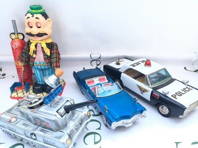 4 X Japanese Battery Operated Tinplate Toys. Including A Gino Neapolitan Balloon Blower (Boxed), A T-5 Tank, Police Car And A Cadillac. No Reserve.