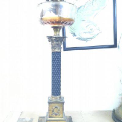 A Victorian brass oil lamp the glass font above a corinthian column .
