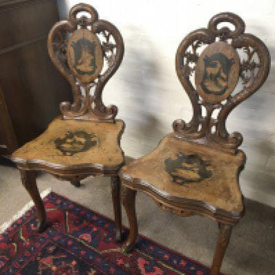 A pair of early 20th Century inlaid and carved Austrian chairs. the backs inlaid with images of Alpine ibex with hinged seats one enclosing a musical box. provenance the chairs with label previously owned by the late Lieutenant Colonel Charles Henry Leet Park MB CM a surgeon with the Indian Medical Service.