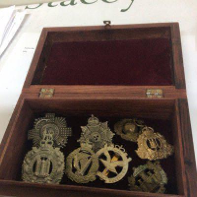 An inlaid hardwood box containing military regimental hat badges.