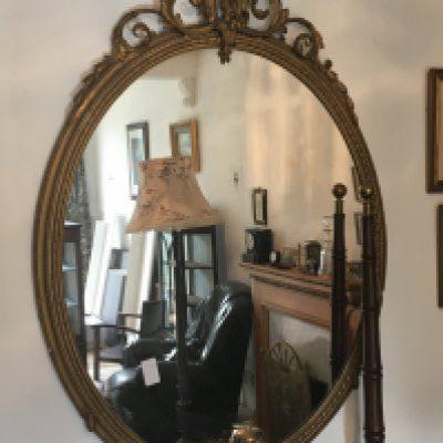 A large late 19th century gilt wood wall mirror of oval shape with applied scroll decoration. Hight 160cm approximately.