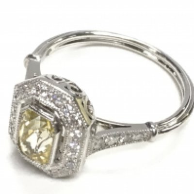 Platinum ring set with a central yellow sapphire surrounded by R/C diamonds with diamond set shoulders and filigree detailing. Yellow sapphire 1.24ct. Diamonds 0.20ct. Ring size Approx M. Postage category A.