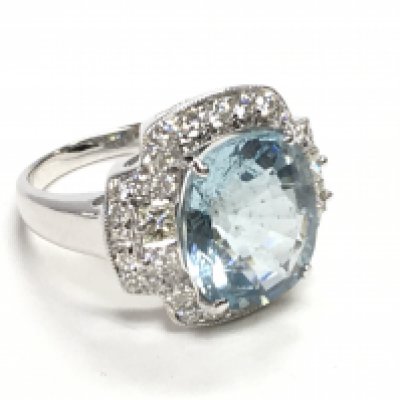 18ct white gold dress ring set with a large oval cushion aquamarine surrounded by Princess cut and RBC diamonds. Aquamarine 6.15ct. Diamonds 1.00ct (RBC 0.64ct, Princess cut 0.36ct) ring size Approx M. Postage category A.
