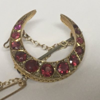 A 9carat gold crescent brooch set with a row of graduating ruby coloured stones weight 3g