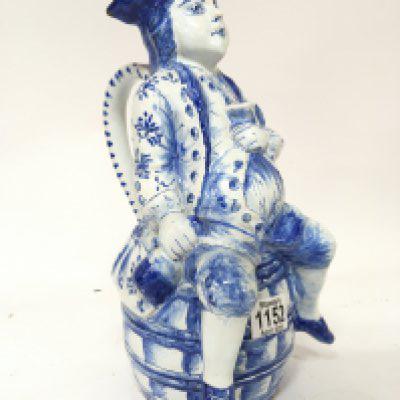 A Delft Character jug a figure with bottle and glass in hand sat on a barrel. Height 34cm makers marks to the base