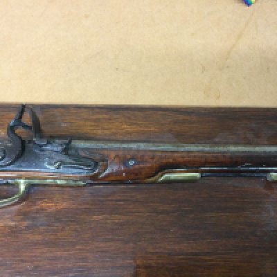 A flintlock pistol with brass mounts fitted in a mahogany plaque .
