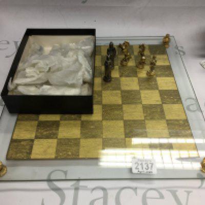 A glass chessboard with silver and gold coloured chess pieces.