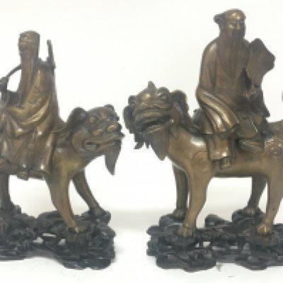 Two conforming 19th century Chinese bronze figures of seated elders on stylised temple dogs on carved hardwood stands height 30cm