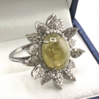 A floral style ring set with a central oval cabochon green tourmaline, with surrounding diamond-set leaves in white metal. Tourmaline 7.18ct. Diamonds 1.11ct. Postage category a