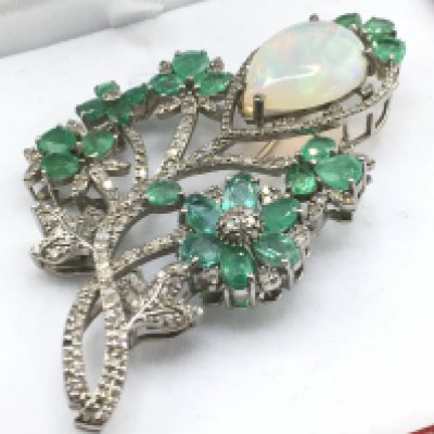 A Foliate bar pin brooch set with a cabochon pear shaped opal, pear shaped emeralds and diamonds, in silver. Opal 7.88ct, emeralds 7.85ct, diamonds 2.08ct. Postage category a