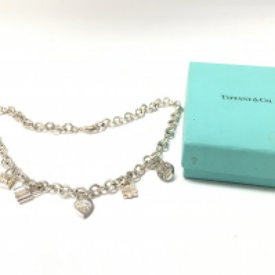 A boxed silver charm necklace marked Tiffany. Postage category a