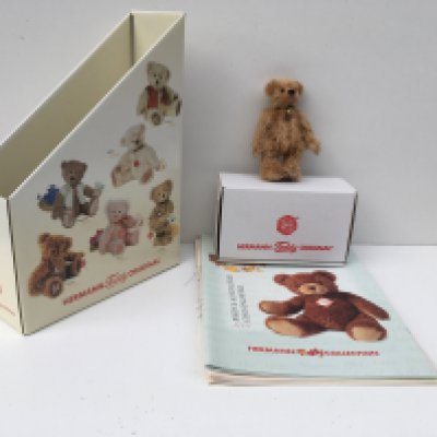 A boxed Herman minature 12 cms brown teddy bear from 2006 with bell on collar. Also includes magazines and storage holder. No reserve