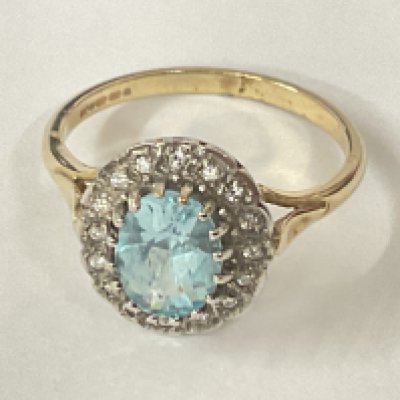 9ct yellow and white gold ring set with central oval blue topaz surrounded by halo of R/C diamonds. Blue topaz 1.10ct. Diamonds 0.08ct. Postage category A.