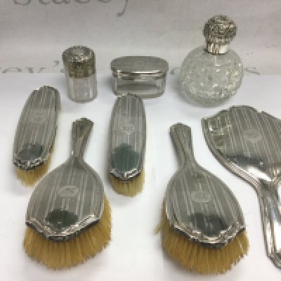 A diver dressing table set comprising a handmirror and brushes, Birmingham hallmarks, plus two silver topped perfume bottles with repousse work decoration and a silver topped tidy jar. Shipping category D.
