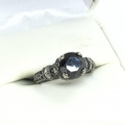 A 10 carat white gold ring set with a 1.25 carat black diamond and smaller white diamonds. Ring size I. Postage cat a