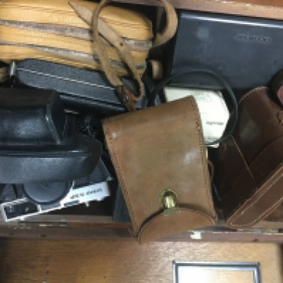 A box containing a collection of cameras a Nikon lens and other accessories.