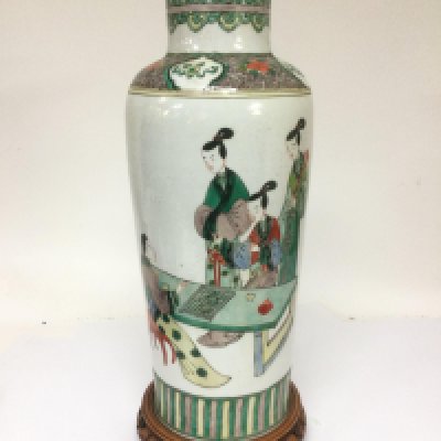 A large Famille vert vase depicting figures in an interior setting and raised on a carved hardwood base, approx height of vase 46cm. Shipping category D.