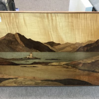 A parquetry panel depicting ocean scenery to include lighthouse with mountains beyond