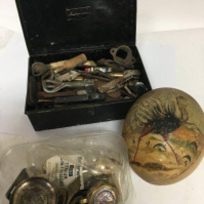 A collection of bottle openers corkscrews an old painted ostrich egg and a tub containing oddments including a trench art lighter.