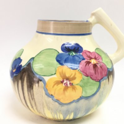 A clarice cliff hand painted pansies pattern jug with an unsual shape. 19cm tall.Slight chip seen on the rim. This lot cannot be posted