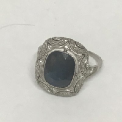 An Art Deco ladies ring set with a good sized deep blue Sapphire with a delicate surround by a delicate pattern of small diamonds. Possibly unmarked Platinum weight 5.5g ring size R. Sapphire approximate surface dimensions 12mmx9mm