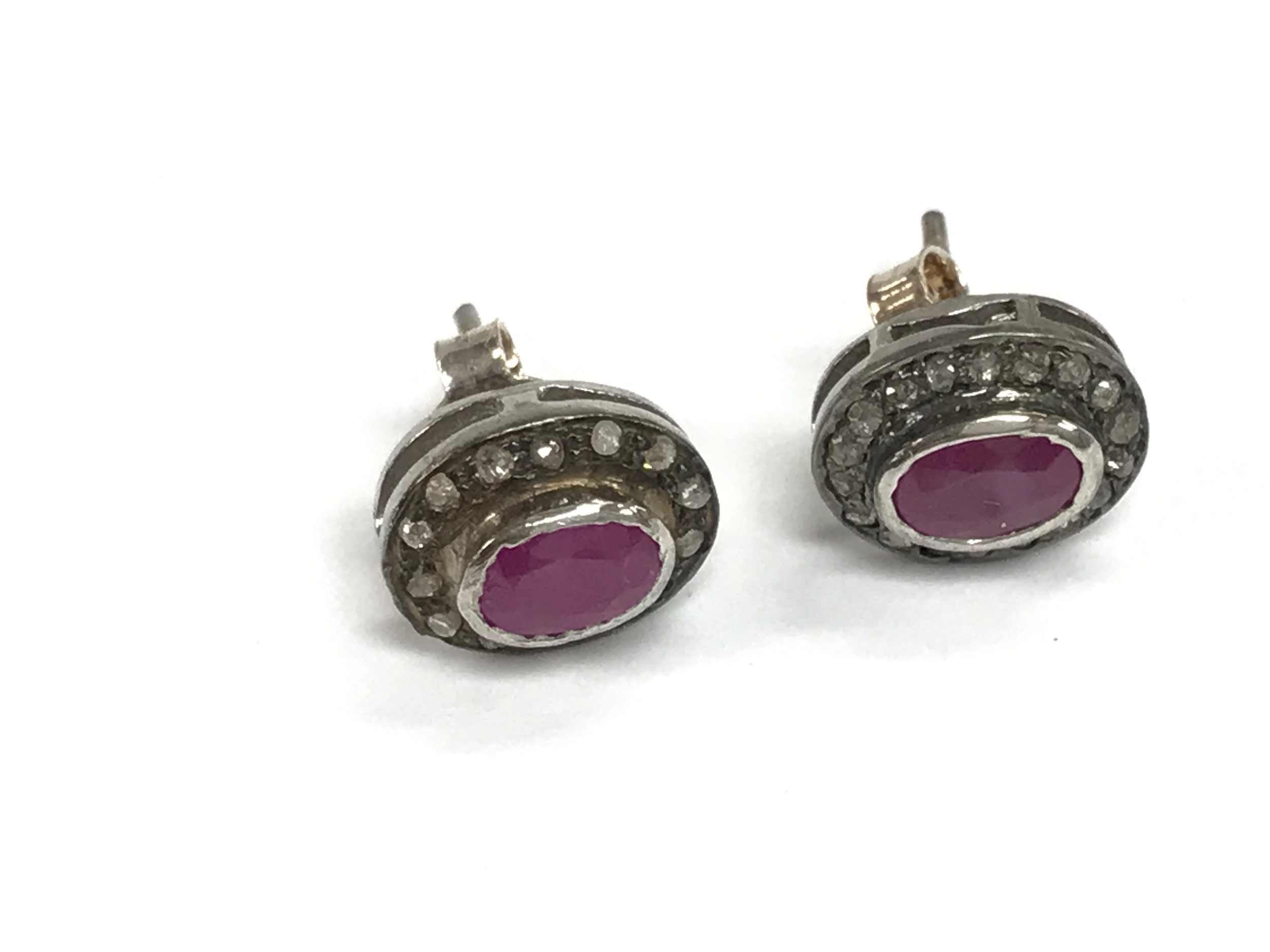 Pair of silver studs set with oval rubies and diamond halos. Rubies approx 0.35ct and diamonds approx 0.15ct.