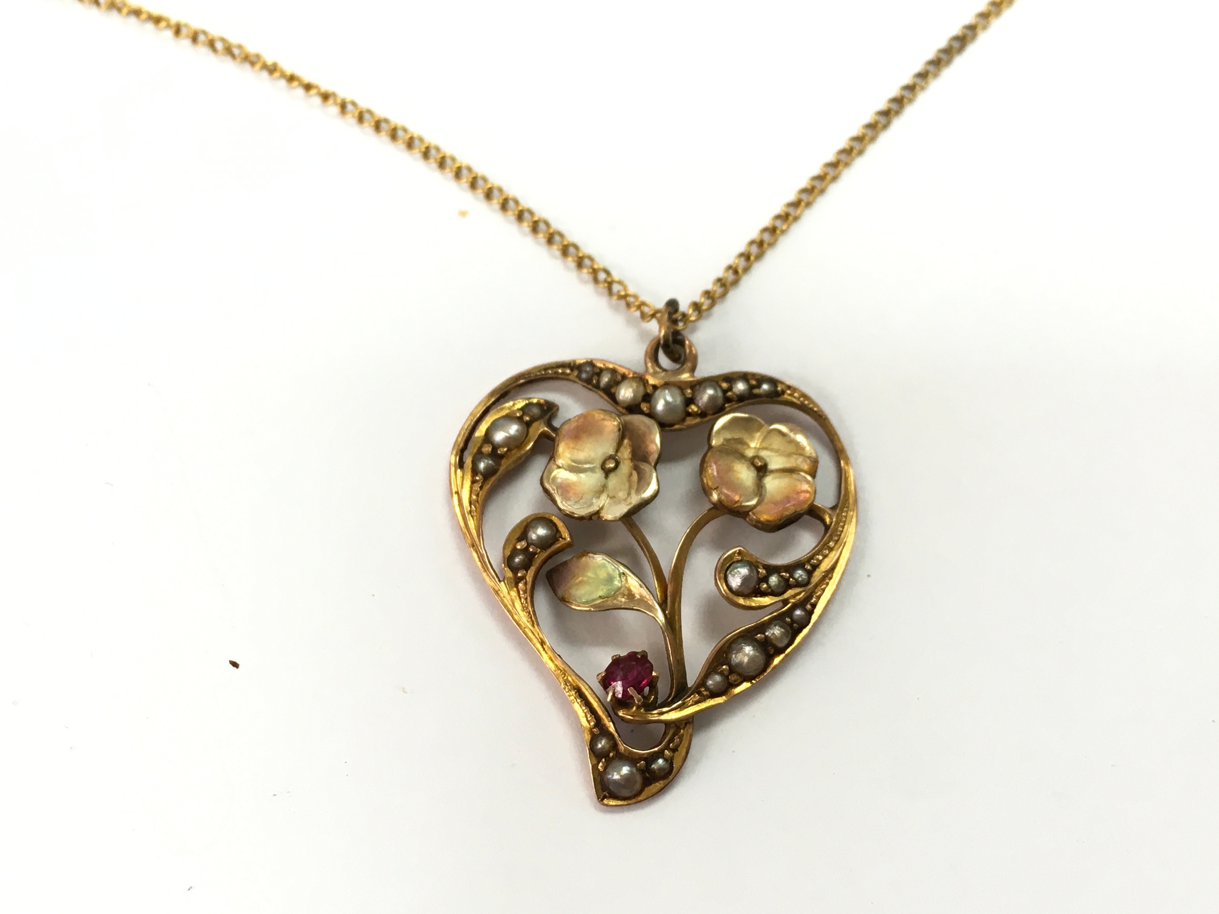 A 9ct gold vintage heart pendant necklace featuring an openwork floral design decorated with small seed pearls and a small red gemstone. 3.4g