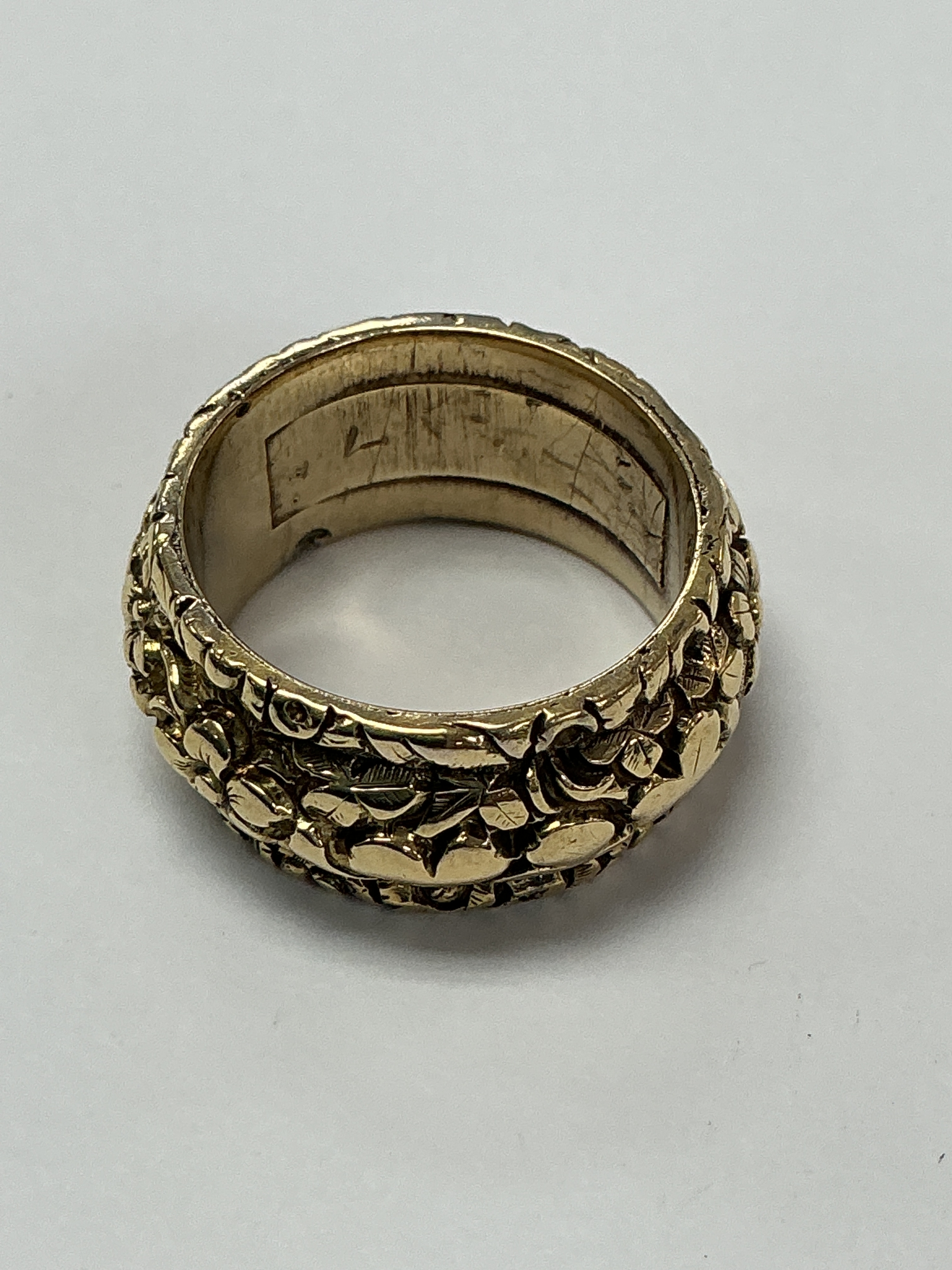 An unmarked yellow gold ring, the thicker band having relief floral decoration. Approx size O.8.91g