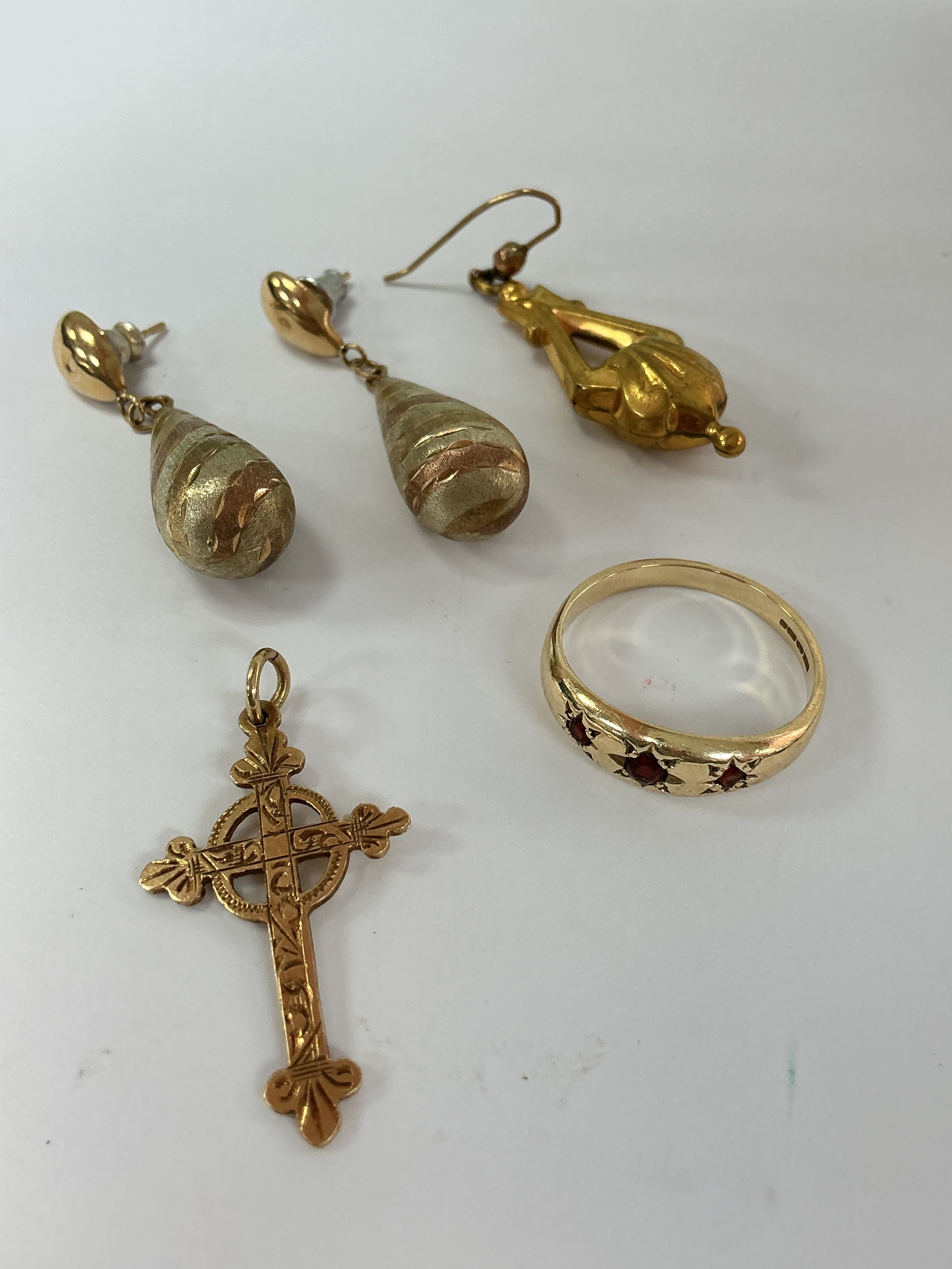 A 9ct gold ring set with probable garnets, a 9ct gold cross, plus a pair of multi tone gold drop earrings and one odd example. 6.86g