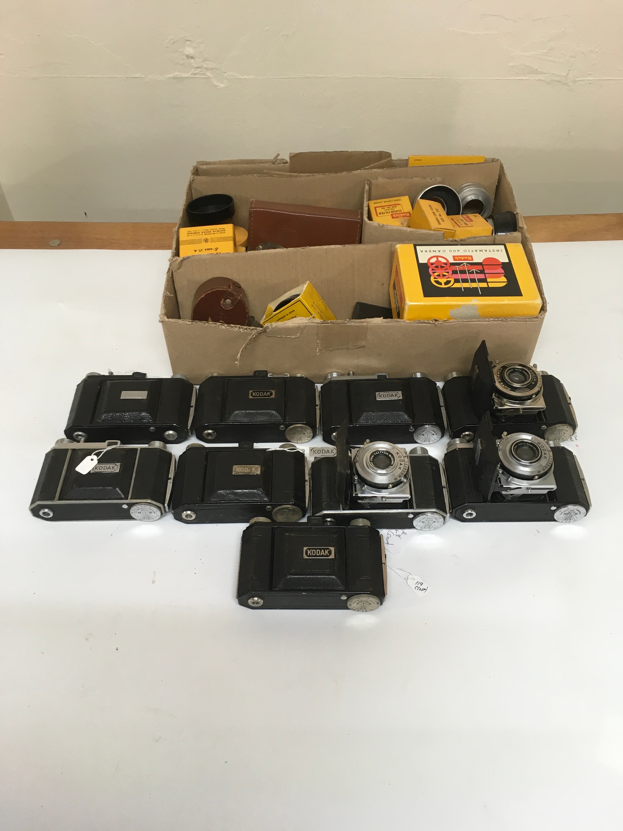 9 Kodak Compur Cameras. 1 box of assorted camera lens accessories and pouches/ boxes.