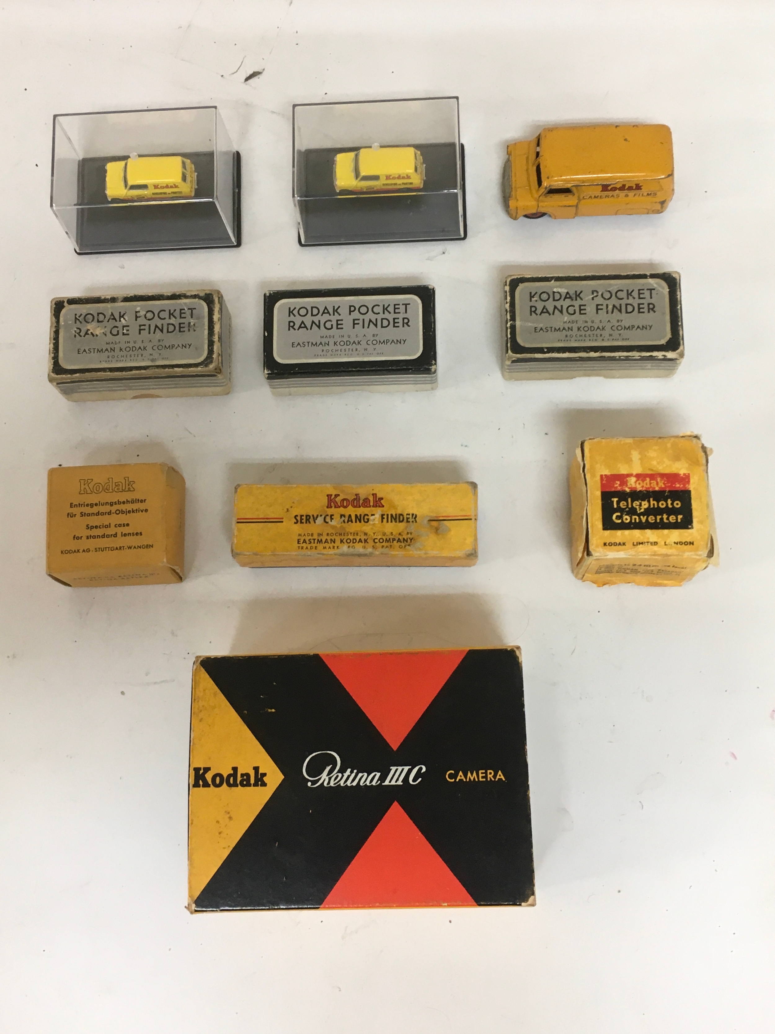An assortment of Kodak advertisement toy cars. Pocket Range finders, Kodak special case for standard lenses, Telephoto Converter, and Kodak Retina III C Camera box with manual, lens equipment inside.