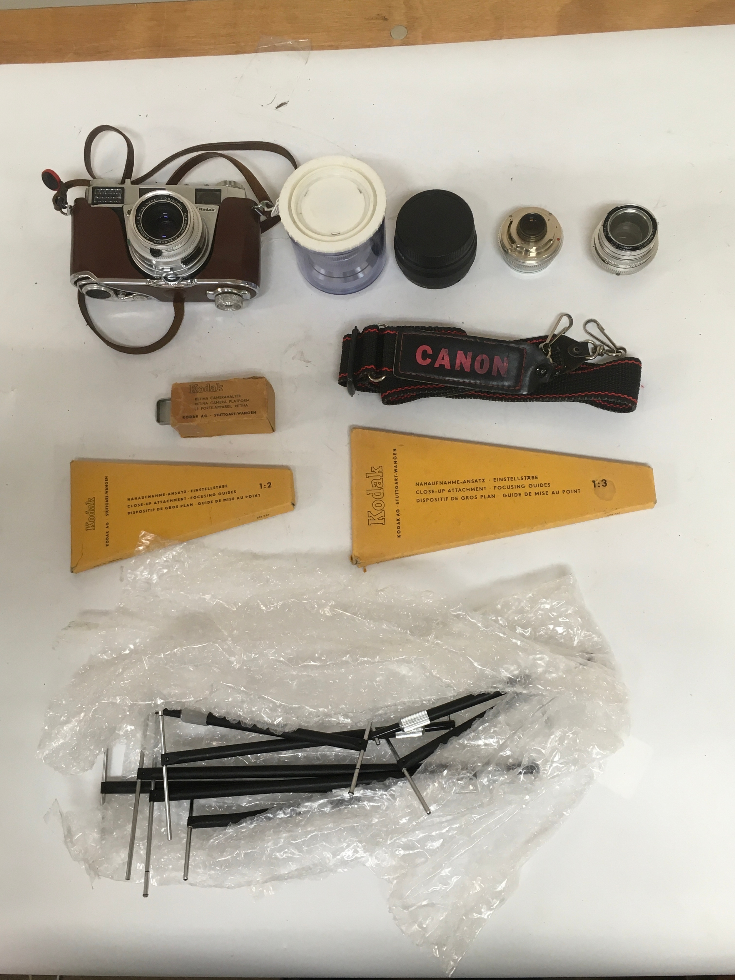 10 items. Kodak Synchro Compur Retina III S with holster strap. Assortment of 4 detachable camera lenses with cover. Canon camera strap. Kodak Retina Camera Platform with box. Several close up focusing guides.