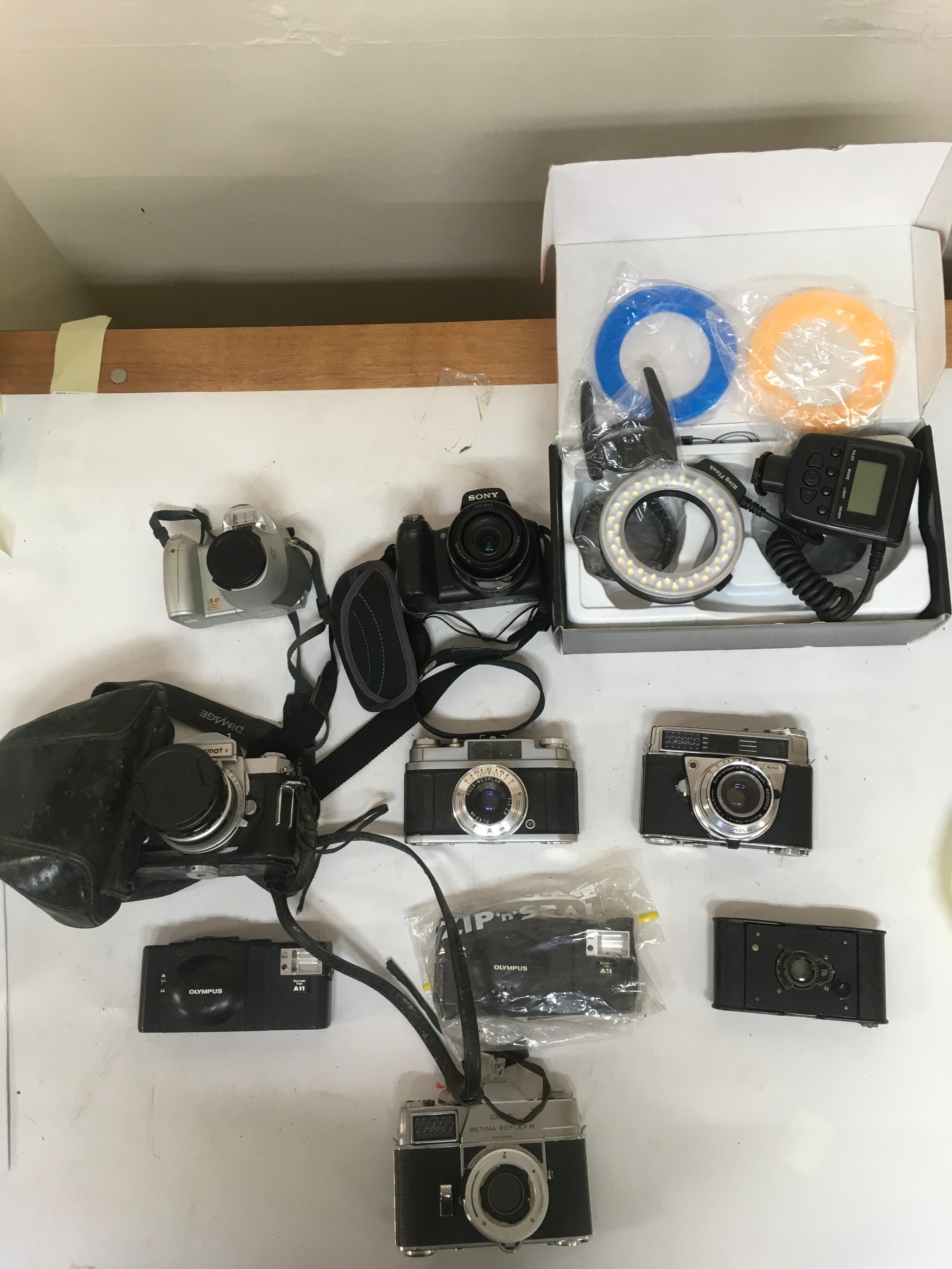 Assortment of 10 modern and period Cameras and LED Ring Flash equipment. 1 pocket Autographic  film camera.2 Olympus  Electric Flash A11 cameras.  2 Kodak cameras. Retina Reflex III & Retina automatic III. 1 Foca-Neoplar. 1 Nikon Nikkormat with holster/ Carrier.1 Sony Video Cameras. 1 Konica Minolta, DIMAGE Z20.